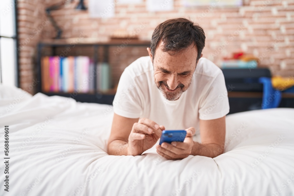 Middle age man using smartphone lying on bed at bedroom Middle age man using smartphone lying on bed at bedroom