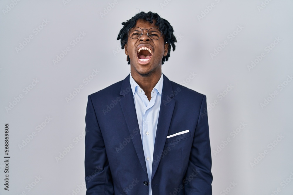 Young african man with dreadlocks wearing business jacket over white background angry and mad screaming frustrated and furious, shouting with anger. rage and aggressive concept. Young african man with dreadlocks wearing business jacket over white background angry and mad screaming frustrated and furious, shouting with anger. rage and aggressive concept.