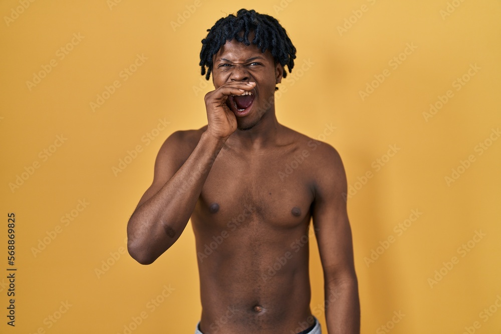 Fototapeta premium Young african man with dreadlocks standing shirtless shouting and screaming loud to side with hand on mouth. communication concept.