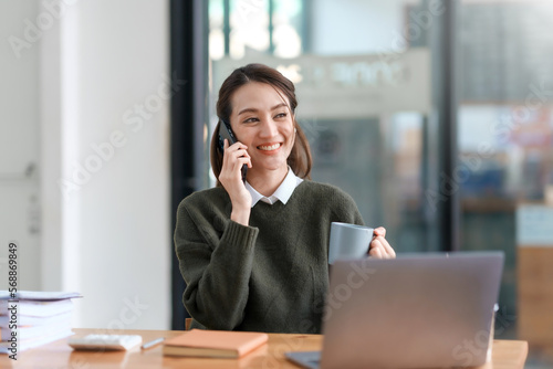 Beautiful smiling Asian businesswoman talking on mobile phone while working in office.