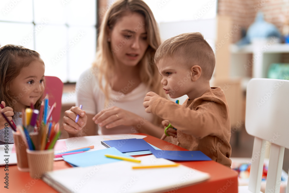 Teacher with boy and girl sitting on table having handcrafts class at kindergarten