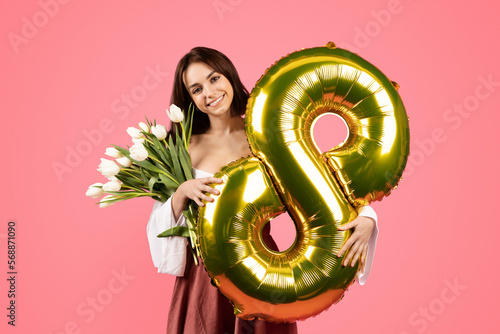 Cheerful young european lady hold bouquet of flowers and balloon number 8, rejoices spring holiday