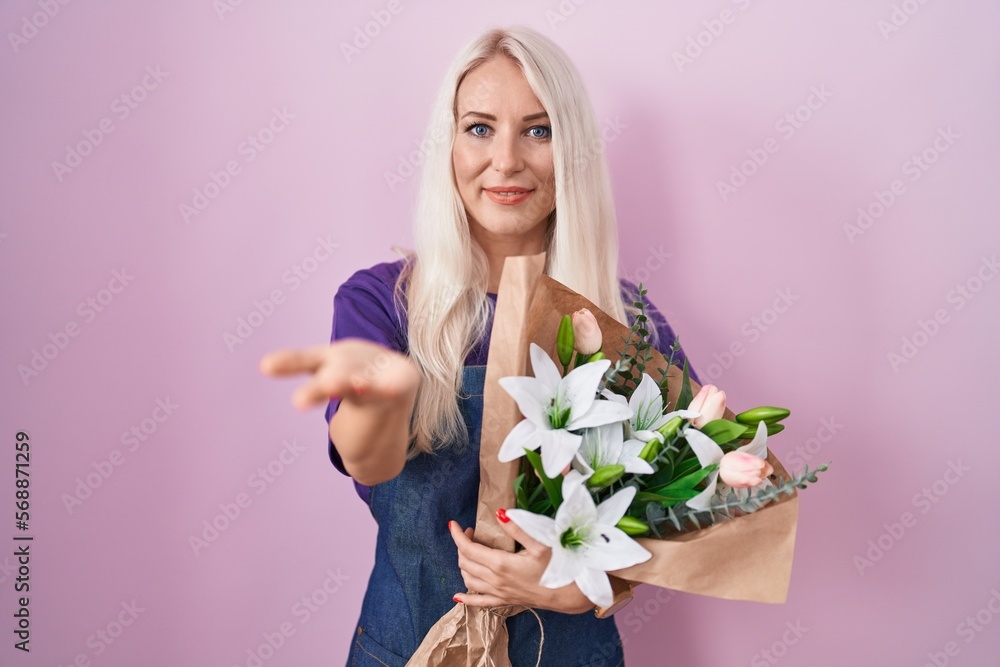 Caucasian woman holding bouquet of white flowers smiling cheerful offering palm hand giving assistance and acceptance.