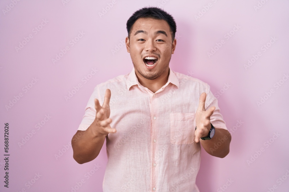 Chinese young man standing over pink background celebrating crazy and amazed for success with arms raised and open eyes screaming excited. winner concept Chinese young man standing over pink background celebrating crazy and amazed for success with arms raised and open eyes screaming excited. winner concept
