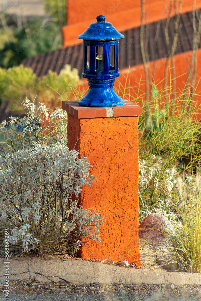 Light post in front yard with orange stucco exterior and slick blue lamp on top with light inside in desert environment Light post in front yard with orange stucco exterior and slick blue lamp on top with light inside in desert environment
