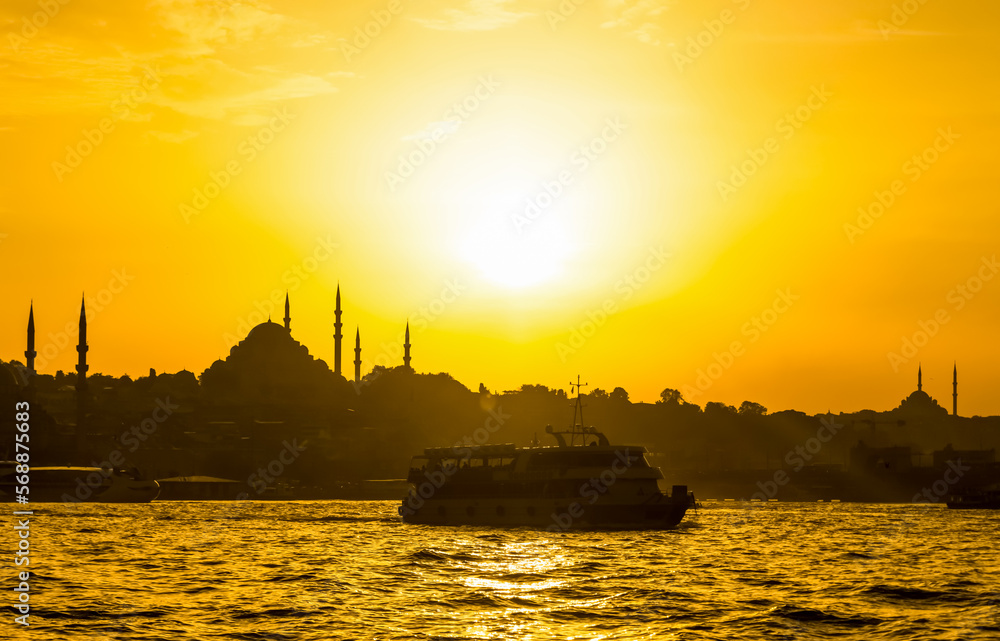 A ferry is seen on Bosphorus in Istanbul, Turkey. Minarets of mosques on the shores of Golden Horn are seen in the background during sunset.