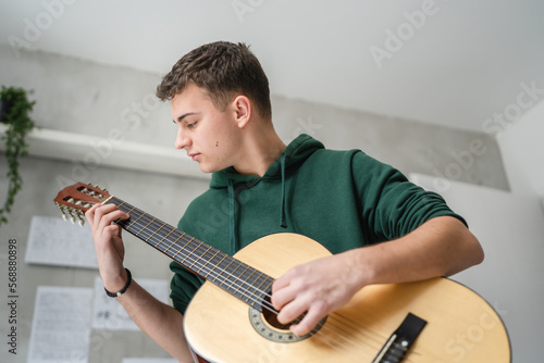 One young man Caucasian teenager sit at home in room playing guitar