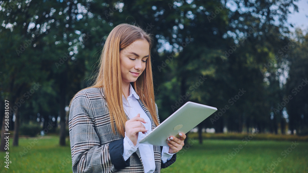 A young girl walks with a tablet in the park. A young girl walks with a tablet in the park.