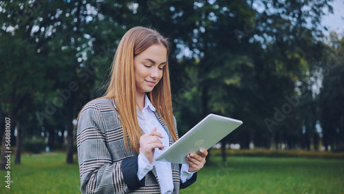 A young girl walks with a tablet in the park.