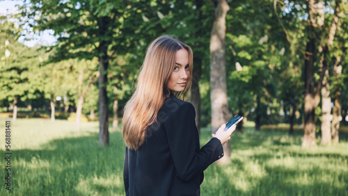 A beautiful girl walks in a city park with a phone.