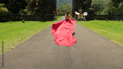 Pretty asian woman walks to balinese gates in long red dress in slowmotion on Hangara gates in Bali Indonesia. High quality fullhd footage
