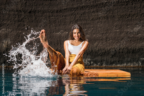 Beautiful woman splashing water on wooden raft in cenote photo