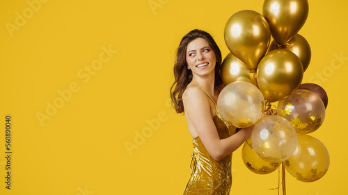 Party time. Charming happy woman in dress holding bunch of balloons over yellow background, panorama with copy space