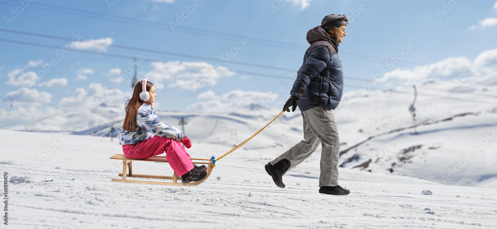 Man in winter clothes pulling a child with a sled on a mountain