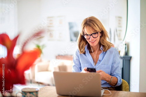 Attractive woman with earphones and mobile phone using laptop at home
