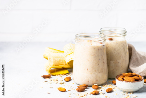 Almond banana smoothie with oat flakes in glass jars at white table.