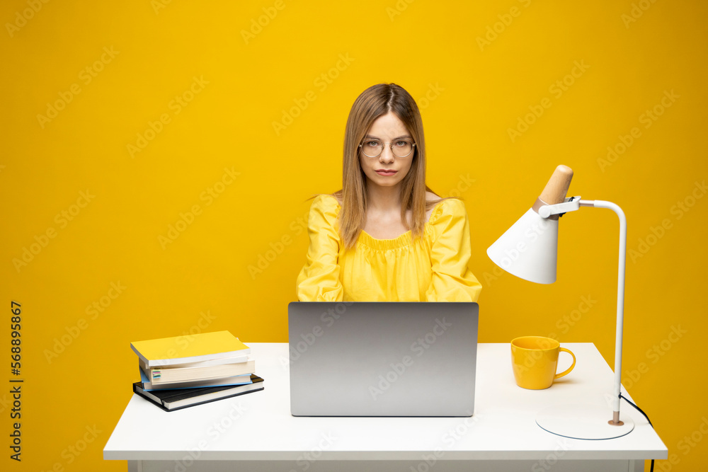 Young blonde freelancer woman in a yellow shirt using laptop for remote work, e-learning at university college, e-banking, online shopping, webinars. Yellow bakcground. Young blonde freelancer woman in a yellow shirt using laptop for remote work, e-learning at university college, e-banking, online shopping, webinars. Yellow bakcground.