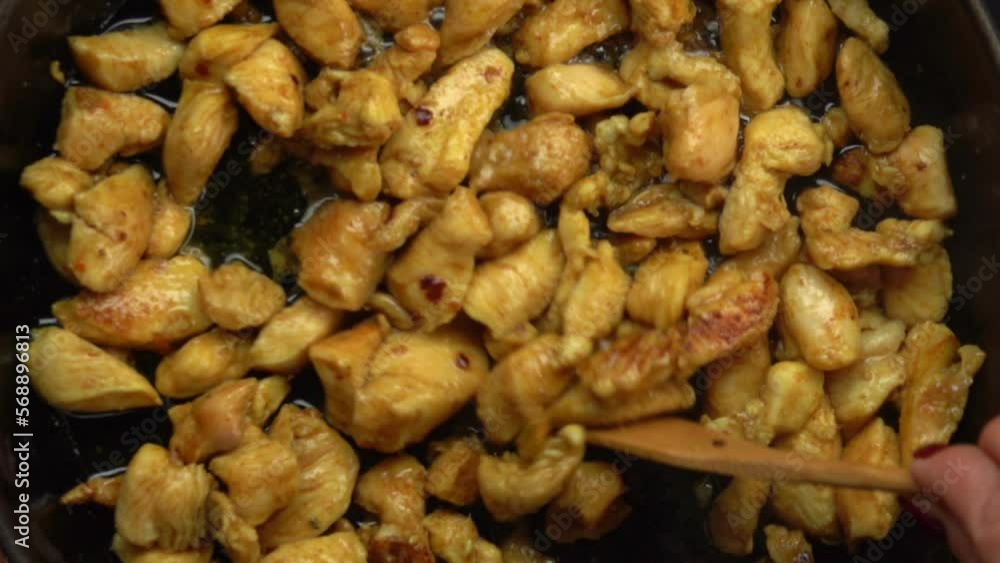 Top close-up view of a wooden spatula spoon stires juicy chicken pieces Top close-up view of a wooden spatula spoon stires juicy chicken pieces