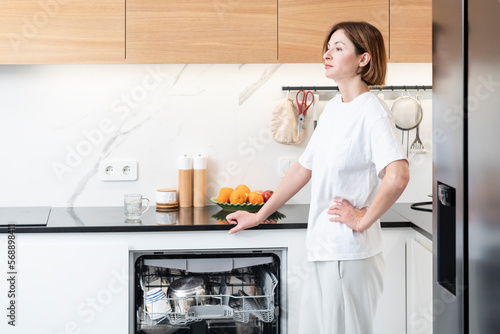 Busy housewife putting dirty plates in dishwasher machine in the kitchen. Household and exhausting cleaning day concept