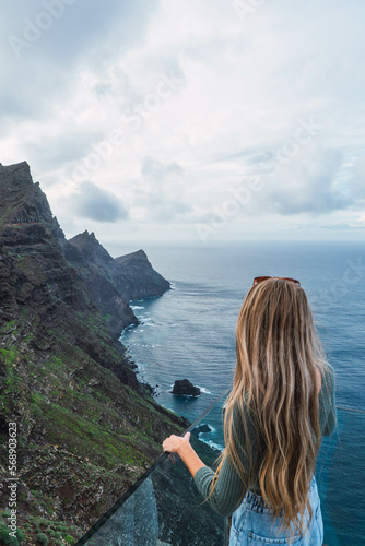 Backwards of woman with blonde hair looking at coastline landscape