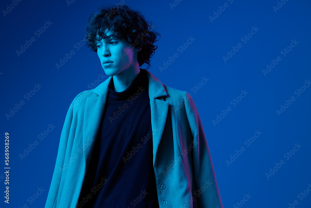 Male fashion model in jacket poses against a dark blue background, neon light, style and trends, mixed light, men's fashion, copy spot