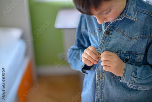 Boy fastens the button of a denim shirt