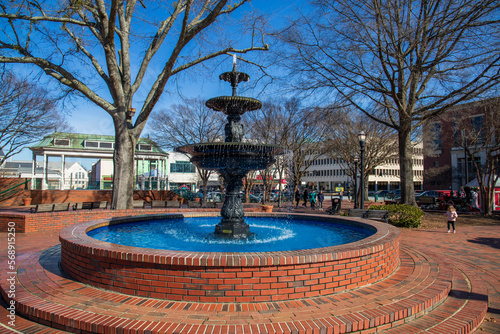 A gorgeous winter landscape at the Marietta Square with red brick footpath, a water fountain, bare trees and lush green plants with a clear blue sky in Marietta Georgia USA photo