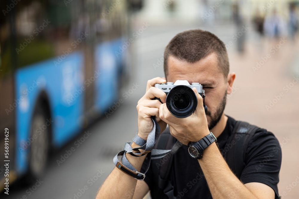 Portrait of young adult caucasian photographer taking a picture with a retro style camera against blurred city street at background Portrait of young adult caucasian photographer taking a picture with a retro style camera against blurred city street at background