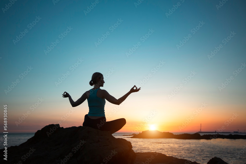 Silhouette of a woman practicing yoga by the sea during sunset.