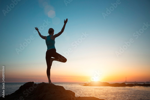Silhouette yogi woman  practicing yoga by the sea during sunset.