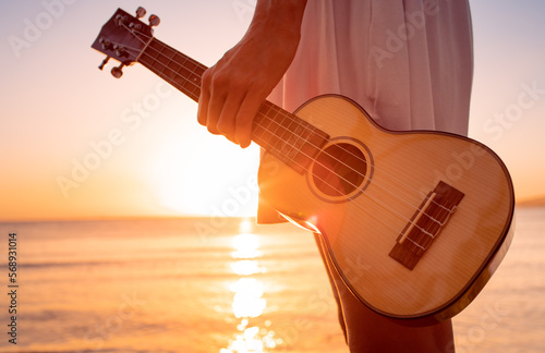 Young female girl holding guitar ukulele on the beach looking out to the sunset. Relax on a summer ocean vacation concept.  photo