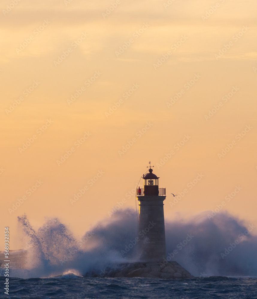 stormy weather, the rough sea are clashing into the lighthouse, during the sunset 
