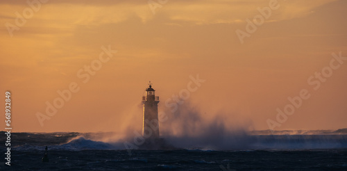 stormy weather, the rough sea are clashing into the lighthouse, during the sunset 