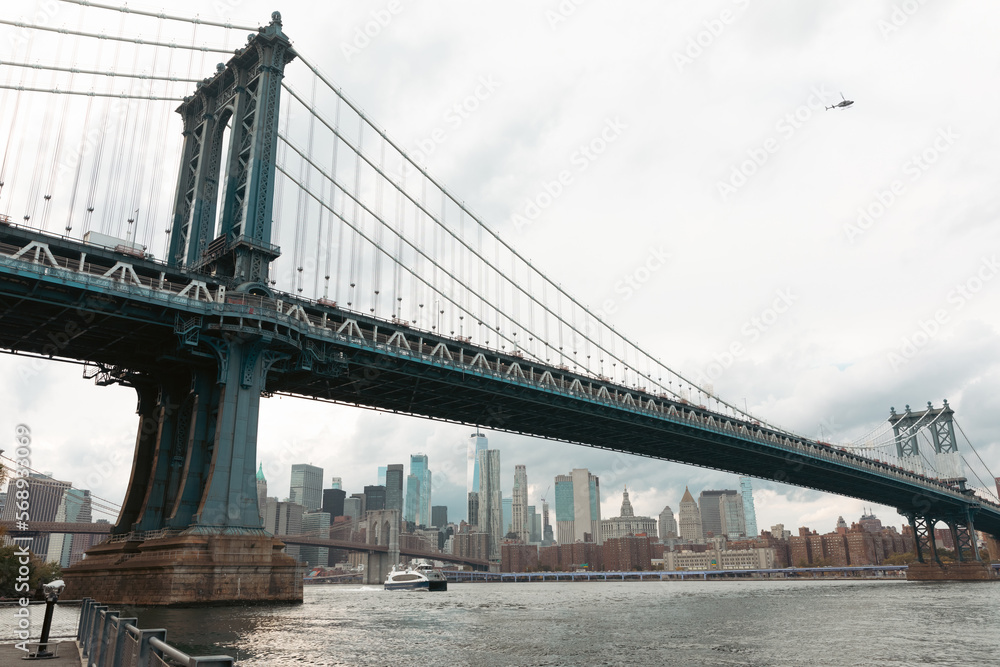 scenic view of Manhattan bridge and modern skyscrapers under cloudy sky in New York City.