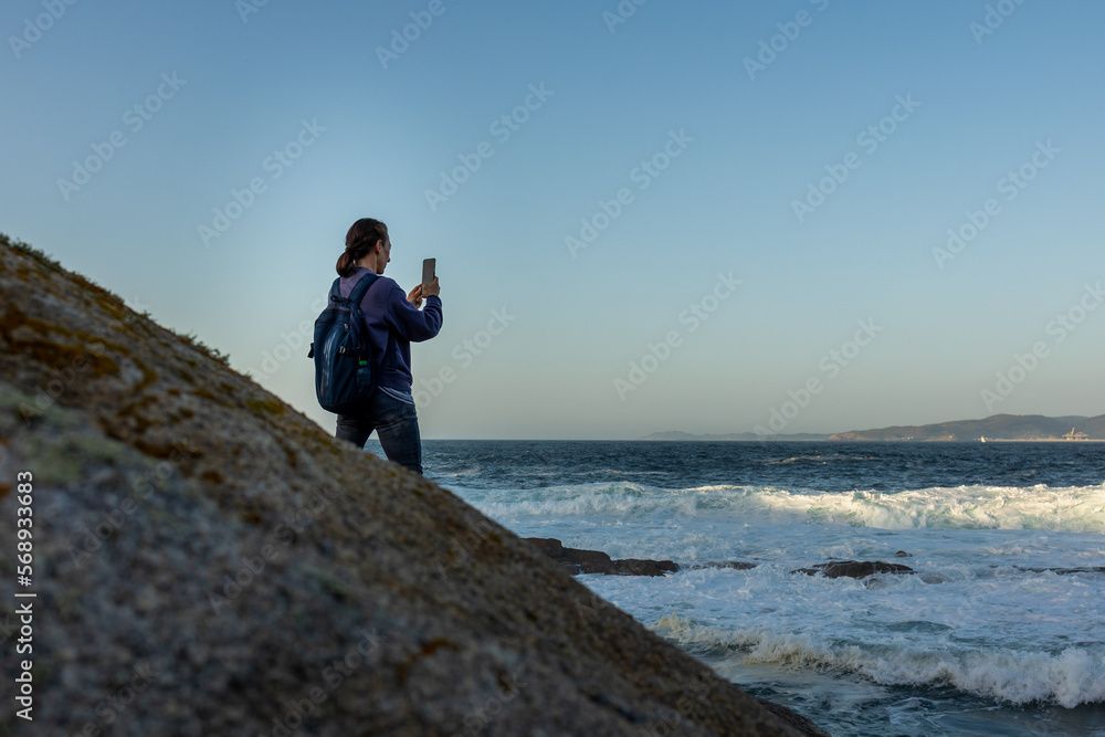 Obraz premium A girl stands on a rock and takes a photo of the ocean