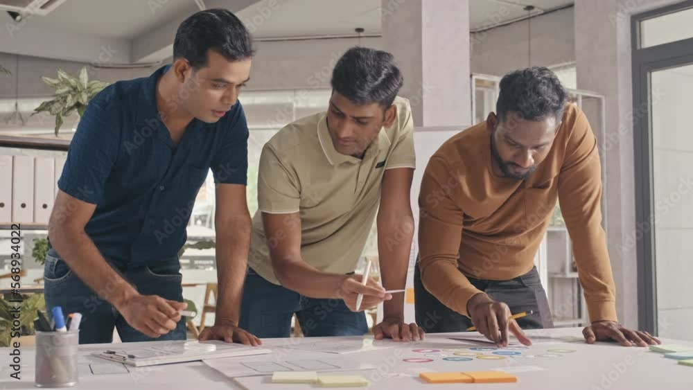 Team of Indian mobile app developers working with paper sketches while discussing layout design in office Team of Indian mobile app developers working with paper sketches while discussing layout design in office