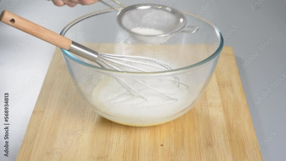 Pour the flour through a sieve into the beaten eggs. Making dough for dessert. High quality 4k footage Pour the flour through a sieve into the beaten eggs. Making dough for dessert. High quality 4k footage