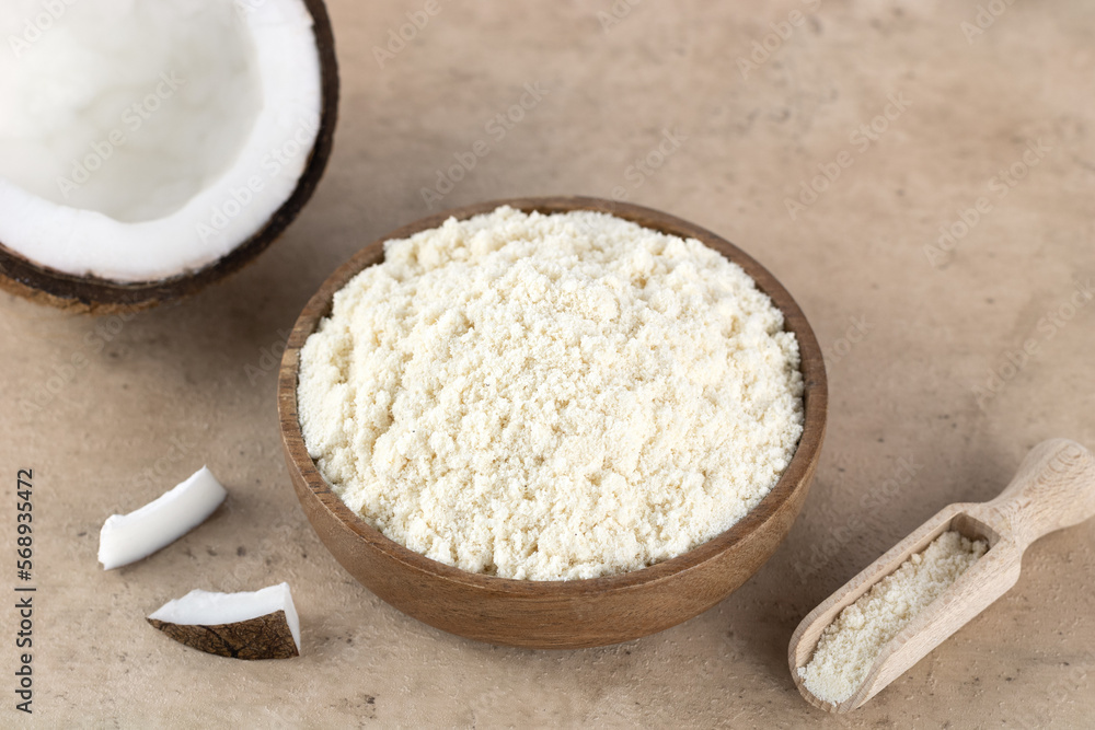 Coconut flour in a wooden bowl and fresh coconuts on a beige background. Baking ingredients. Gluten free food