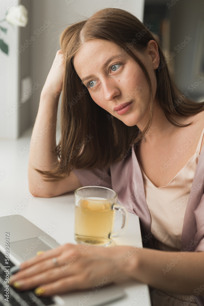 Young woman wears sleeping clothes working on laptop computer while sitting at living room and drinking tea - social network and working at home concept Young woman wears sleeping clothes working on laptop computer while sitting at living room and drinking tea - social network and working at home concept