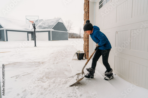 A child pushing a shovel hard to get snow off the ground.  photo