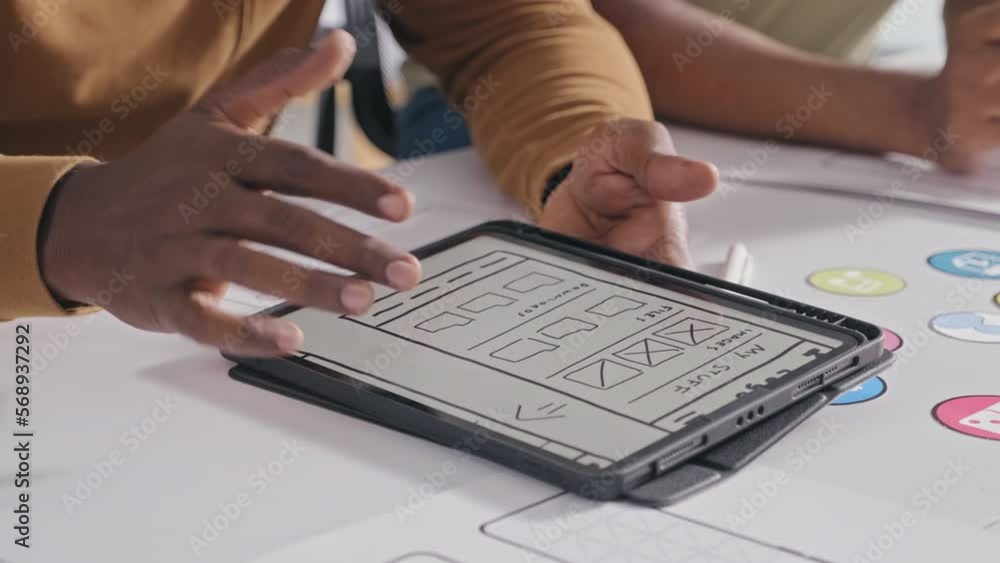 Close up shot of hands of mobile software developer discussing app layout on digital tablet with colleagues while working together on UX design at office desk Close up shot of hands of mobile software developer discussing app layout on digital tablet with colleagues while working together on UX design at office desk