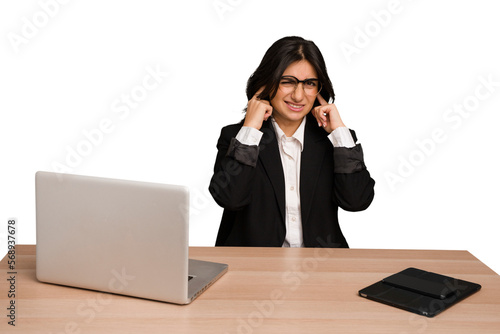 Obraz na plátně Young indian woman in a table with a laptop and tablet isolated covering ears with fingers, stressed and desperate by a loudly ambient