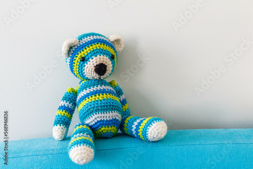Bright knitted striped teddy bear sitting on the back of the bed © Dolia