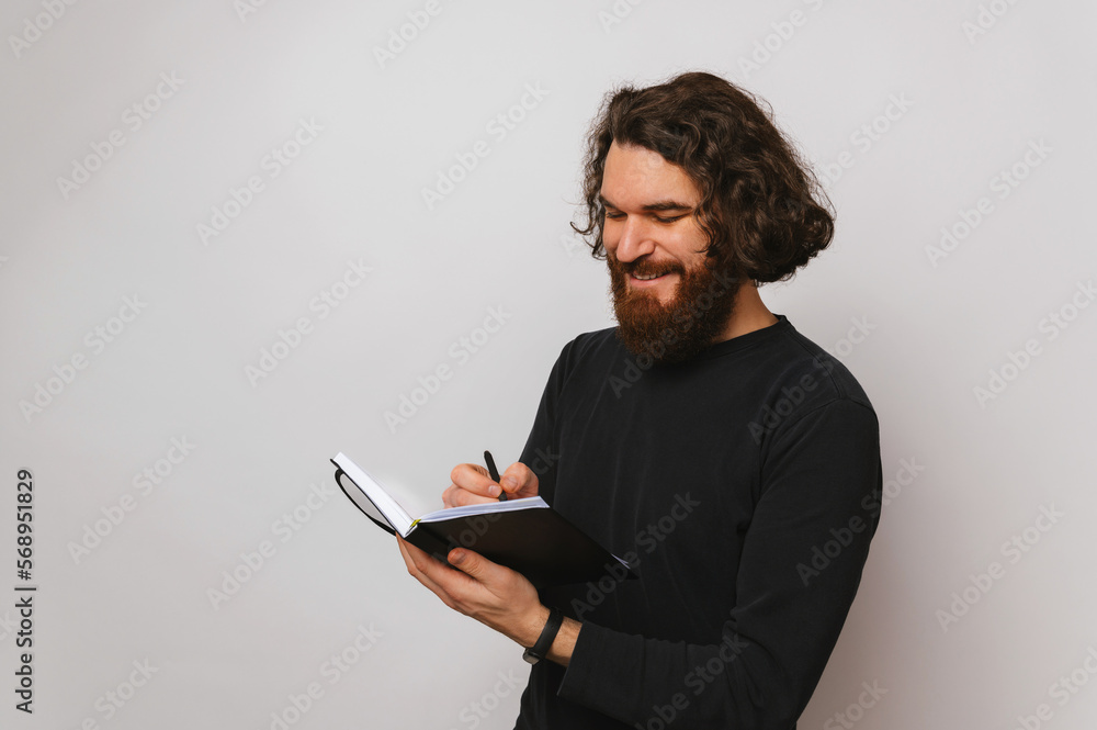 Confident smiling bearded man is writing in his journal the plan of the day. Confident smiling bearded man is writing in his journal the plan of the day.