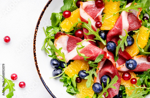 Gourmet salad with smoked duck, oranges, blueberries, cranberries, arugula and lettuce, white table background, top view, close-up