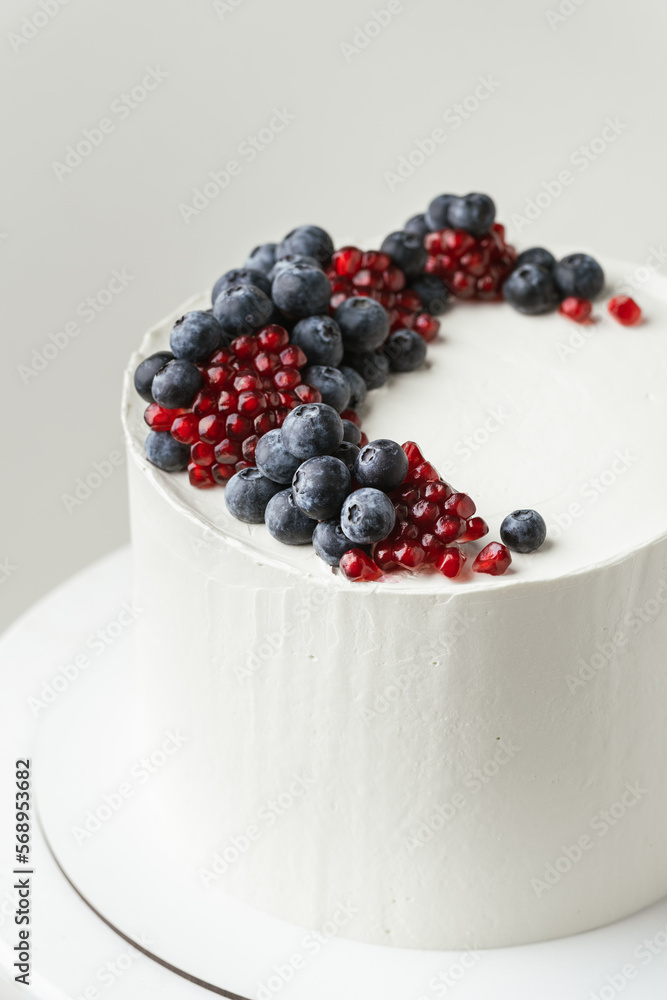 Birthday cake with white cream cheese frosting decorated with fresh blueberries and pomegranate. Elegant summer cake with red and blue berries on the white background Birthday cake with white cream cheese frosting decorated with fresh blueberries and pomegranate. Elegant summer cake with red and blue berries on the white background