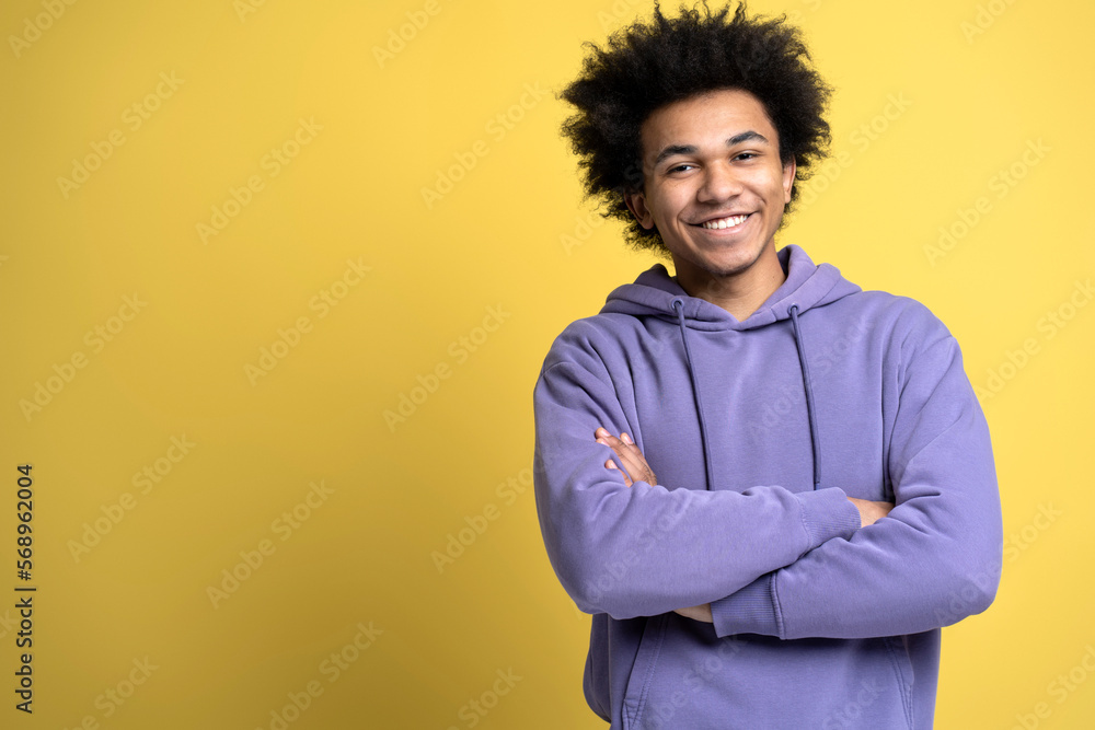 Handsome smiling African American man with arms crossed isolated on yellow background, copy space. Happy smart student wearing stylish purple hoodie looking at camera, studio shot. Education concept Handsome smiling African American man with arms crossed isolated on yellow background, copy space. Happy smart student wearing stylish purple hoodie looking at camera, studio shot. Education concept