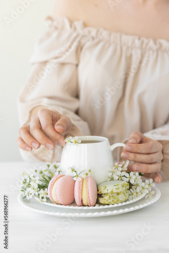 Traditional delicious French dessert - sweet homemade macarons on a vintage plate. Colourful tasty macaroons served on a white china with herbal tea. Decorated with fragile cherry tree flowers.