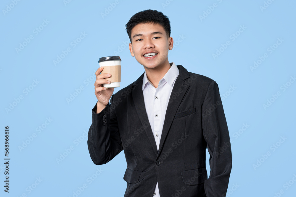 Young handsome asian businessman smiling while holding hot coffee in takeaway paper cup isolated on blue light background. Business Person concept. Young handsome asian businessman smiling while holding hot coffee in takeaway paper cup isolated on blue light background. Business Person concept.