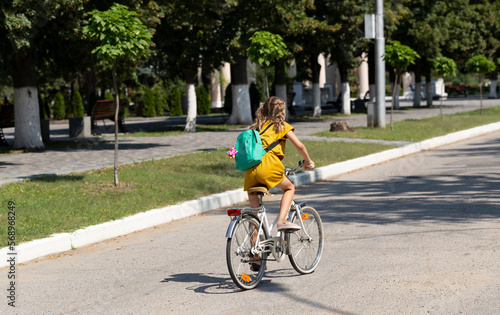 A little girl rides a bicycle on the city road. View from the back.